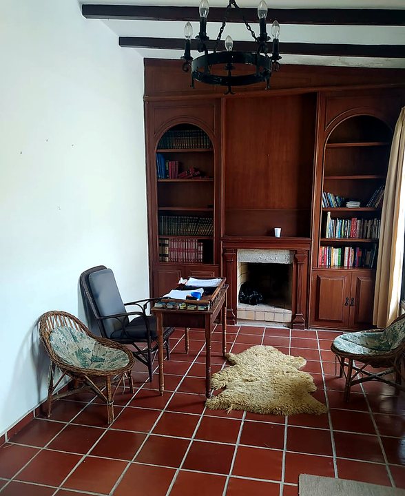 Sala de leitura com estante de livros, mesa e lareira